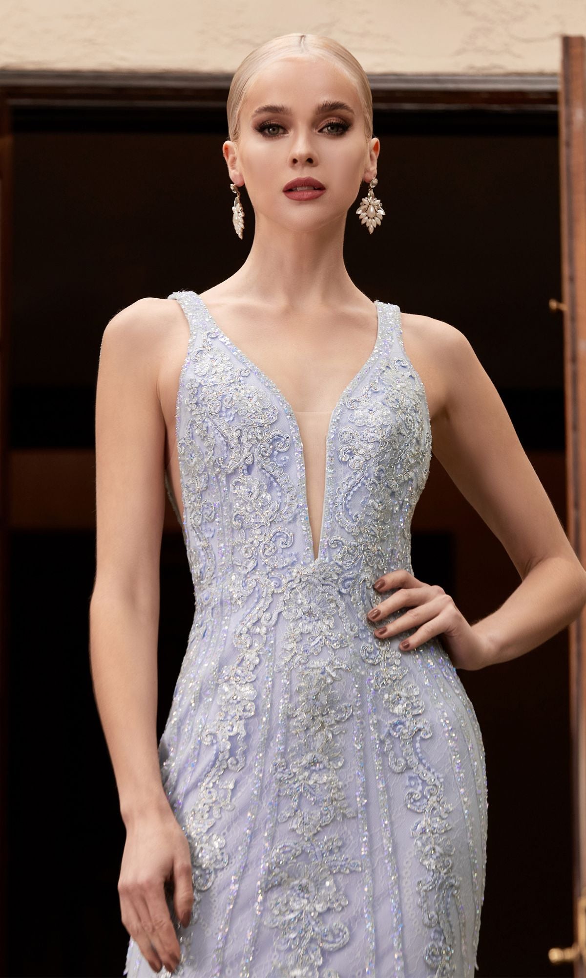 Woman wearing the Floral-Beaded Deep V-Neck Prom Dress CD981, a sleeveless light blue gown with beaded floral details, standing with one hand on her hip and accessorized with dangling earrings.
